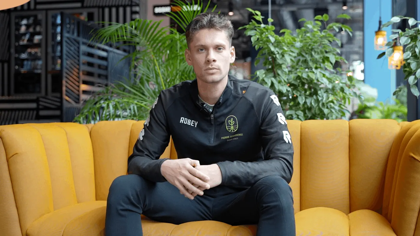 Mees Gootjes in een zwart Voetbal Dream Coach trainingsjack, zittend op een gele bank